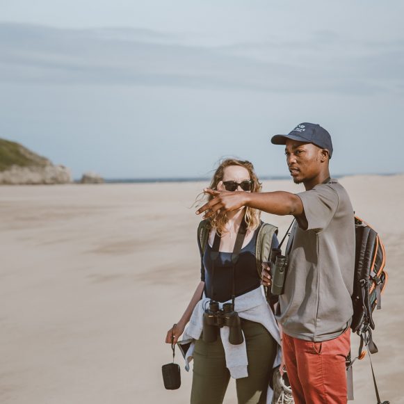 Guide pointing out the view to a hiker on the beach at Robberg