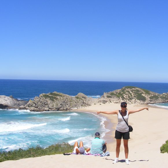 Hiker with arms outstretched on the sand bar between Robberg and The Island
