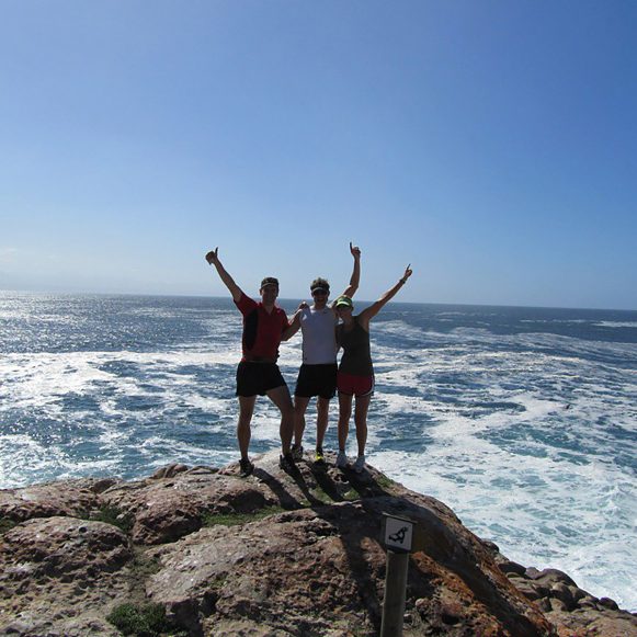 Three hikers celebrating on the rocks above the waves at Robberg